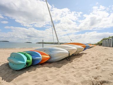 Kayaks lying on sand near the beach with water and islands in the background at Bywyd Da 232 Cae Du in Abersoch