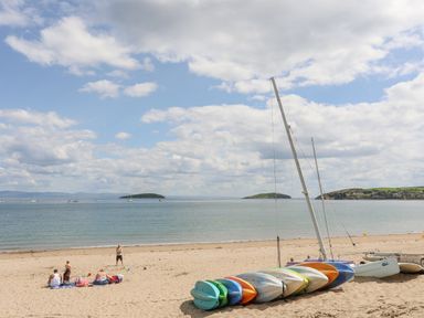 A sandy beach with people sitting and small colorful boats lined up near the shore at Bywyd Da 232 Cae Du in Abersoch