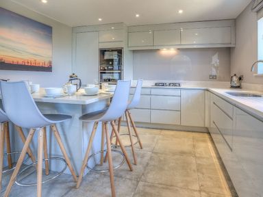 A modern kitchen with a dining island with chairs and white cabinets at Cromlin Glas in Abersoch