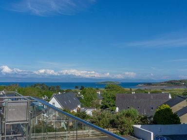 A view of houses trees and the sea with an island in the background at Cromlin Glas in Abersoch