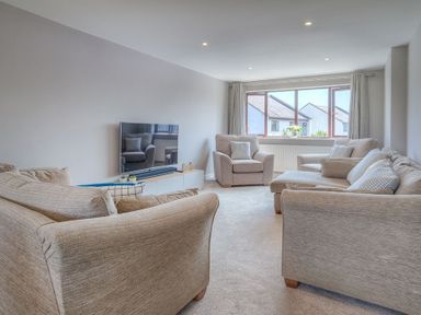 A living room with beige sofas a television and a large window at Cromlin Glas in Abersoch