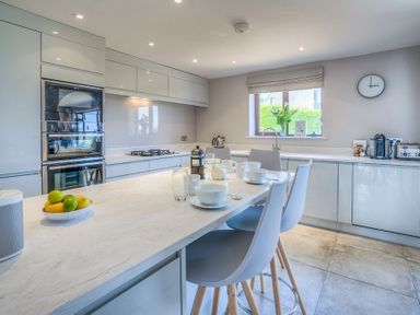 A kitchen with a marble countertop island and stools cups and bowls on the counter at Cromlin Glas in Abersoch
