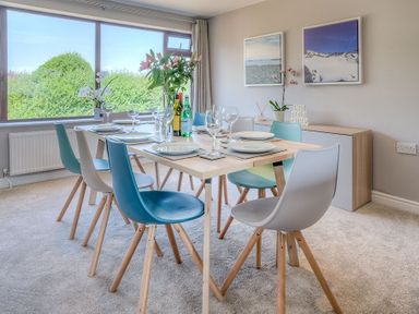 A dining room with a table set for six and large window showing greenery at Cromlin Glas in Abersoch