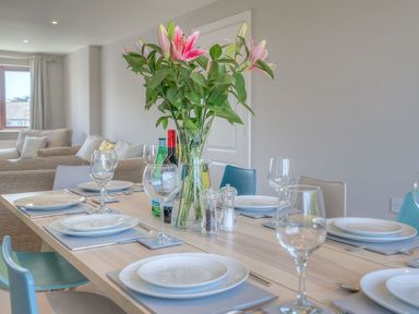 A dining table set with plates wine glasses cutlery and a vase with flowers in a living room at Cromlin Glas in Abersoch