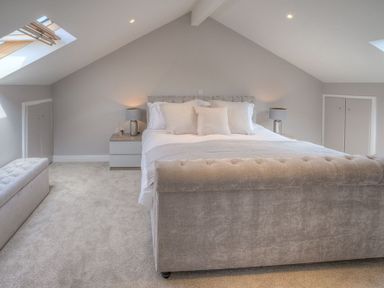 A bedroom with a double bed bedside tables lamps and a storage bench under skylights at Cromlin Glas in Abersoch
