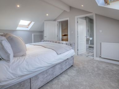A bedroom with a bed pillows and blanket with two doors one leading to a bathroom at Cromlin Glas Abersoch