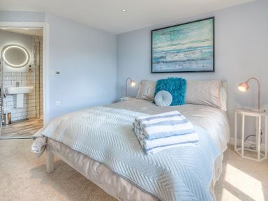 A bedroom with a double bed towels on the bed beside two bedside tables with lamps and a bathroom visible through an open door at Cromlin Glas in Abersoch