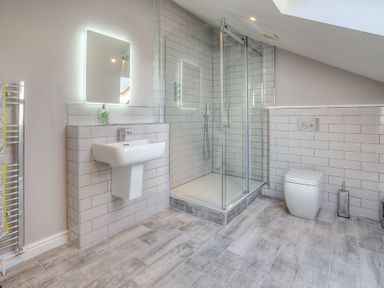 A bathroom with a shower enclosure mirror sink toilet and towel rail at Cromlin Glas in Abersoch