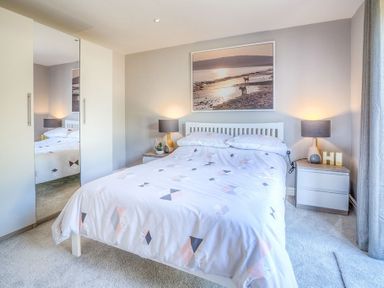 A bedroom with a bed bedside tables lamps and a wardrobe with mirrored doors at Cromlin Glas in Abersoch