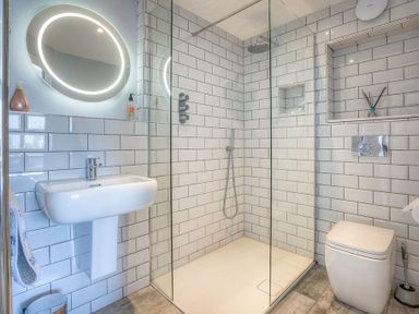 A bathroom with a glass shower enclosure a sink a toilet and a round illuminated mirror at Cromlin Glas in Abersoch
