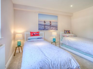 A bedroom with two single beds bedside tables with lamps and a large beach photo on the wall at Cromlin Glas in Abersoch
