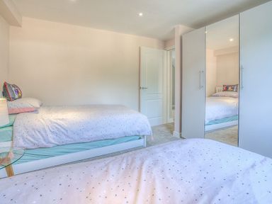 A bedroom with two single beds a lamp a glass side table and a wardrobe with mirrored doors at Cromlin Glas in Abersoch