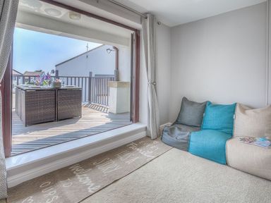 An interior room with a low sofa and open glass door leading to a balcony with a table set for dining at Cromlin Glas in Abersoch
