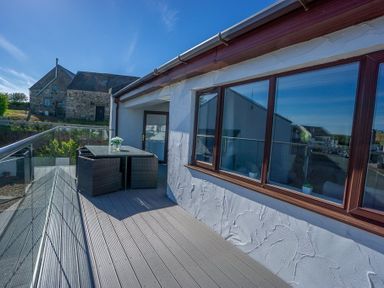 A balcony with a table and chairs outside a building with large windows at Cromlin Glas in Abersoch