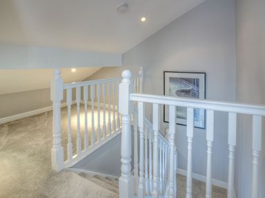 A staircase with white balusters and grey carpet with a framed picture on the wall at Cromlin Glas in Abersoch