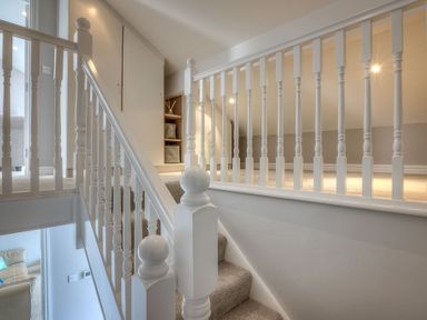 A carpeted staircase with white wooden railings and a small storage area under the sloping ceiling at Cromlin Glas in Abersoch