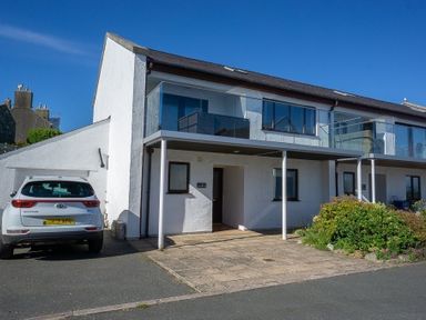 A white two story house with balconies and a parked car at Cromlin Glas in Abersoch