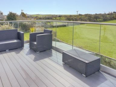 An outdoor patio with two armchairs a sofa and a table with glass railing overlooking green fields at Eleri in Abersoch