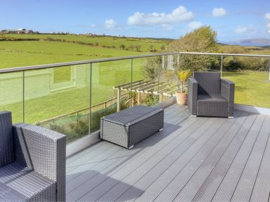 A balcony with two rattan chairs and a rattan table overlooking green fields at Eleri in Abersoch