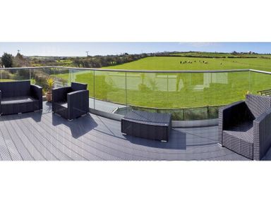 A balcony with black outdoor furniture and glass railing overlooking fields with cows at Eleri in Abersoch