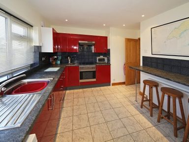A kitchen with red cabinets a sink oven microwave and two stools at a counter at Eleri in Abersoch