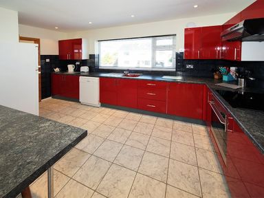 A kitchen with red cabinets black countertops tiled floor and a large window at Eleri in Abersoch