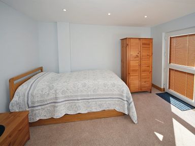 A bedroom with a bed covered with a quilt a wooden wardrobe a wooden chest of drawers and windows with blinds at Eleri in Abersoch