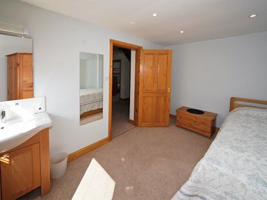 A bedroom with a bed a wooden chest a wooden door and a sink with a mirror at Eleri in Abersoch