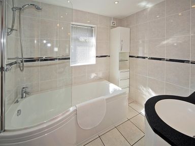 A bathroom with a bathtub shower unit white cabinet and a sink at Eleri in Abersoch