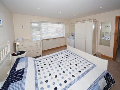 A bedroom with a bed covered in a blue and white polka dot quilt next to a dresser and wardrobe at Eleri in Abersoch