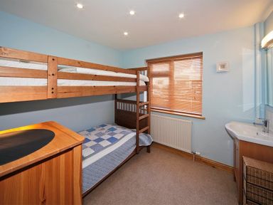 A bedroom with a wooden bunk bed a wooden chest of drawers a window with blinds and a sink at Eleri in Abersoch