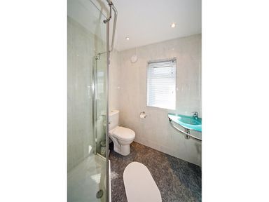 A bathroom with a shower, toilet, window with blinds, and a wall-mounted sink at Eleri in Abersoch