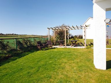 A garden area with grass lawn a wooden pergola two wooden chairs and two small tables at Eleri in Abersoch