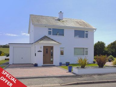 A two-story white house with a garage and a driveway with potted plants at Eleri in Abersoch