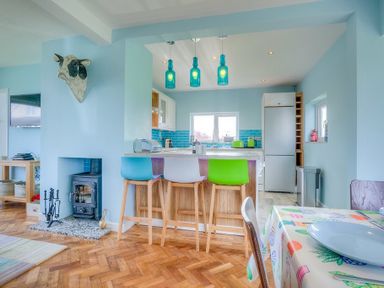 Kitchen and dining area with wooden floor and colorful chairs at Gilfach in Abersoch