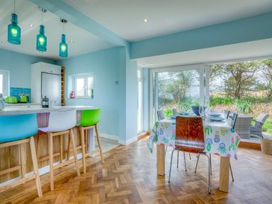 A kitchen and dining area with bar stools and a large window overlooking a garden at Gilfach in Abersoch