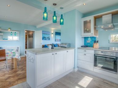 A kitchen with white cabinets blue pendant lights and a dining area at Gilfach in Abersoch