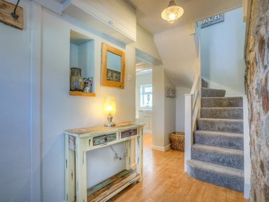 A hallway with a wooden console table holding a lamp and a mirror above near carpeted stairs and a stone wall at Gilfach in Abersoch