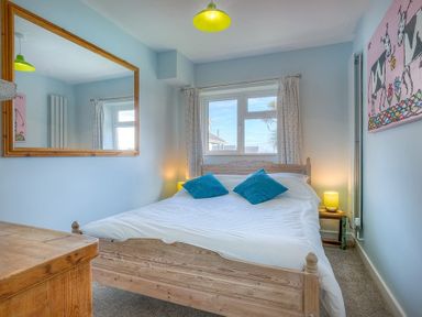 A bedroom with a wooden bed frame blue pillows bedside tables with lamps a large wall mirror and a painting at Gilfach in Abersoch