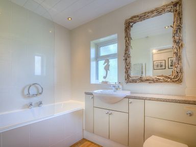 A bathroom with a bathtub a sink a window and a mirror with a wooden frame at Gilfach in Abersoch