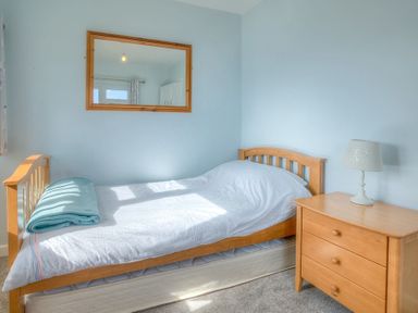 A small bedroom with a single bed a blue blanket a wooden dresser with a lamp and a mirror on the wall at Gilfach in Abersoch