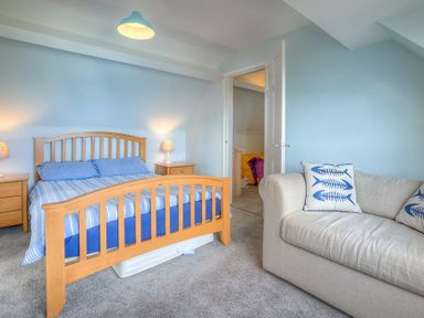 A bedroom with a wooden bed and blue bedding next to a beige couch with fish patterned pillows at Gilfach in Abersoch