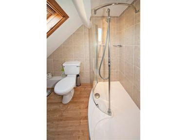 A bathroom with a toilet a shower with glass door and wooden floor at Gilfach in Abersoch