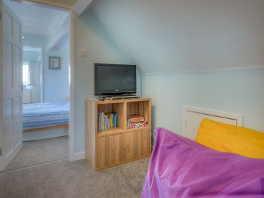 A small room with a wooden cabinet holding a television and books a purple bean bag and an open door showing a bedroom at Gilfach in Abersoch