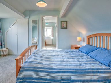 A bedroom with a wooden bed and striped blue bedding a bedside table with a lamp and a built in wardrobe at Gilfach in Abersoch