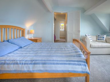 A bedroom with a wooden bed with blue striped bedding a nightstand with a lamp and a white sofa with patterned pillows at Gilfach in Abersoch