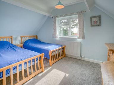 A bedroom with two wooden beds with blue bedding a window with curtains and a wooden dresser at Gilfach in Abersoch