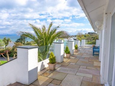 A terrace with potted plants glass railing and blue bench overlooking the sea at 3 Madoc View in Bwlchtocyn near Abersoch