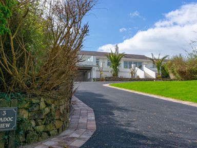 A driveway leading to a white house with palm trees and a green lawn at 3 Madoc View Bwlchtocyn near Abersoch