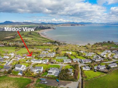 An aerial view of a coastal residential area with houses greenery and a beach at 3 Madoc View in Bwlchtocyn near Abersoch
